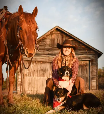 Lisa in front of a barn with herding dogs and a horse